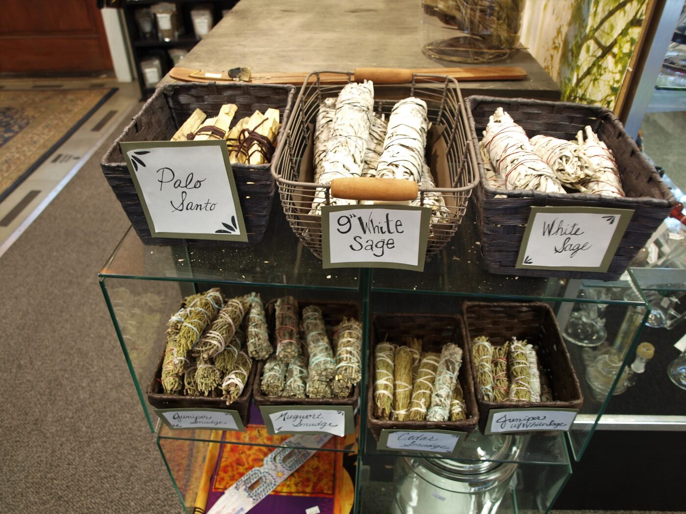 A retail display of white sage bundles and palo santo in baskets at Herb Stomp